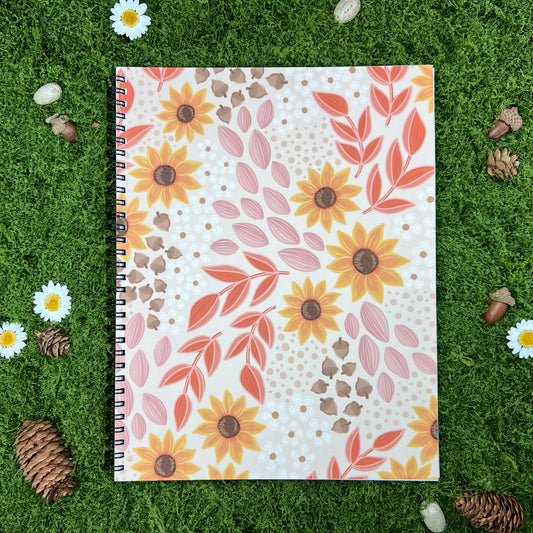 A spiral notebook with a floral pattern of sunflowers and leaves in warm fall colors, set against a beige background. The style is playful and whimsical, with a touch of vintage charm.