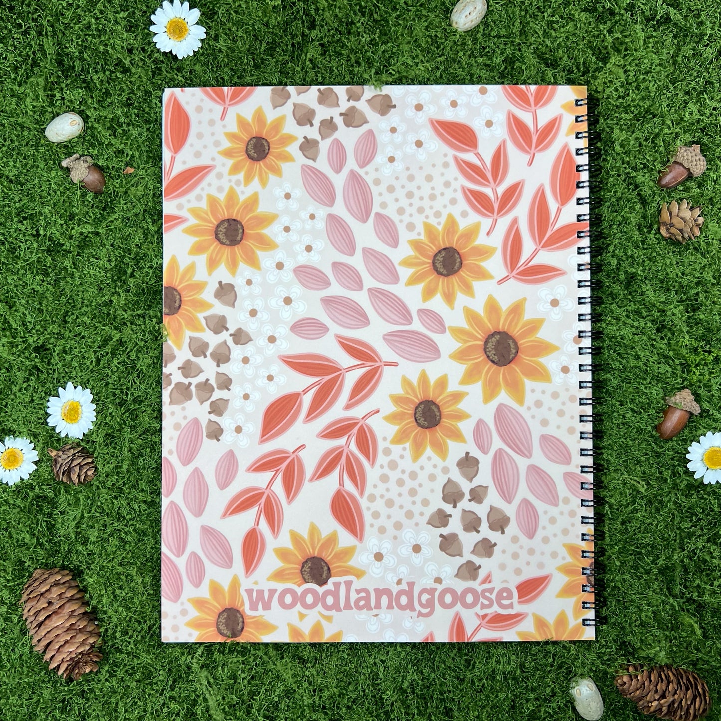 The back of A spiral notebook with a floral pattern of sunflowers and leaves in warm fall colors, set against a beige background. The style is playful and whimsical, with a touch of vintage charm.